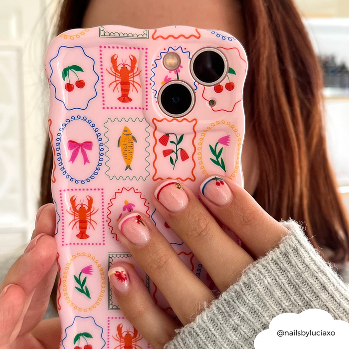 Hand with floral nails holds Coconut Lane Dolce Vita wavy phone case featuring lobsters, cherries, and flower prints.