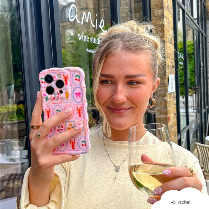 Smiling woman taking a selfie outdoors, holding a phone with a wavy patterned Dolce Vita case by Coconut Lane.