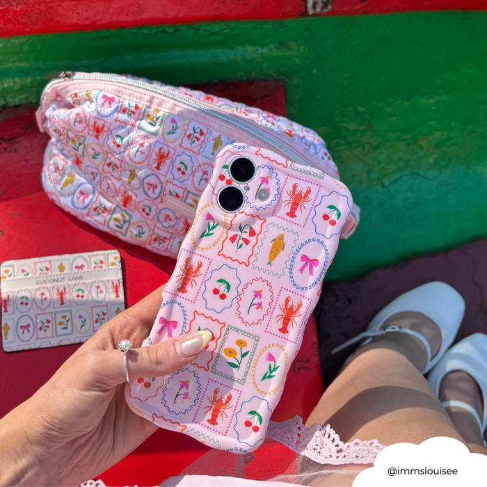 Hand holding a wavy-patterned Dolce Vita phone case, with matching pink bag and cardholder next to it.