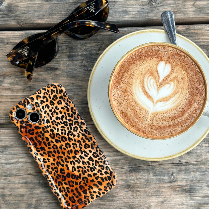 Leopard print wavy phone case, latte with heart art, and sunglasses on a wooden table.