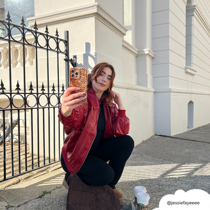 Woman in a red jacket takes a selfie with a Coconut Lane leopard print wavy phone case outside a white building.
