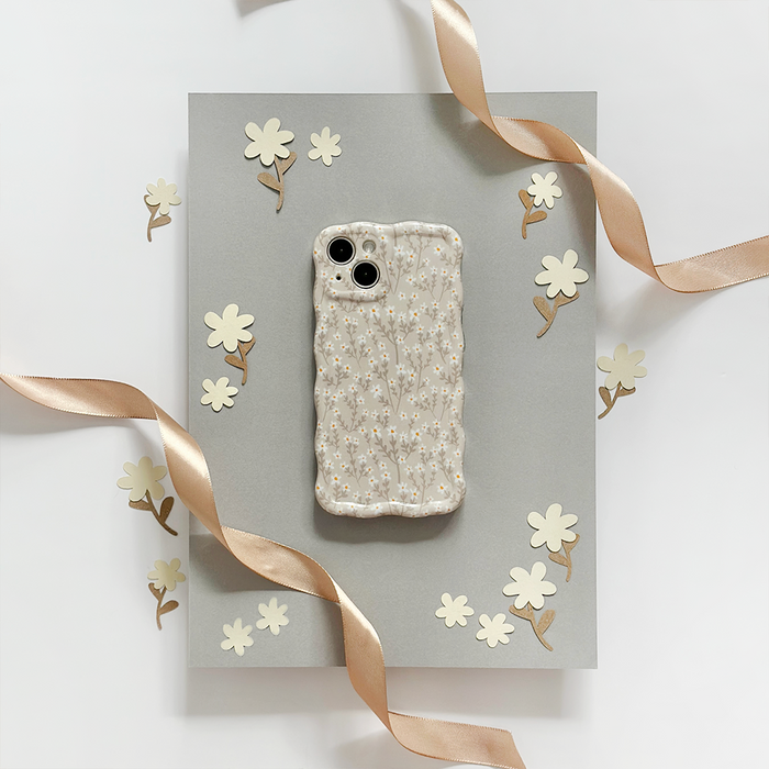 Wavy phone case with nude floral design by Coconut Lane, shown on gray board with paper flowers and gold ribbon accents.