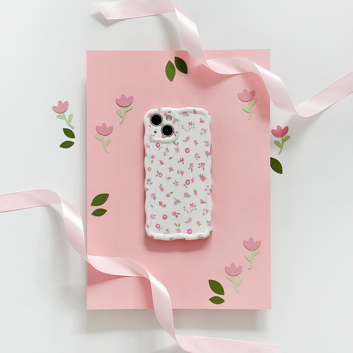 Pink phone case with wavy edges and watercolour floral design, displayed on pink paper with ribbon and flower accents.