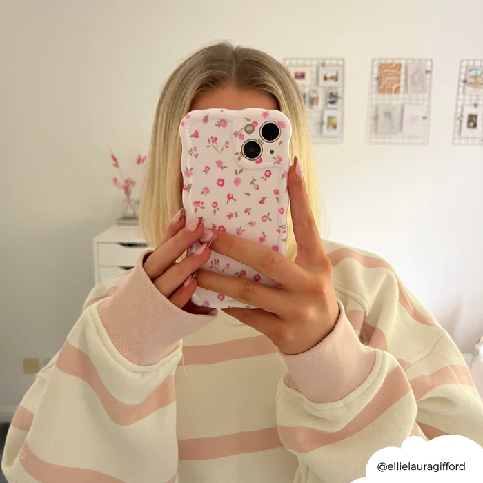 Person in a pink and white striped sweater holding a phone with a wavy, pink floral case in a mirror selfie.