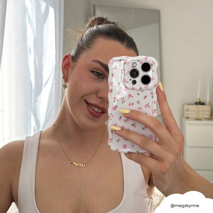 Woman in a white top takes a mirror selfie holding a pink floral wavy phone case.